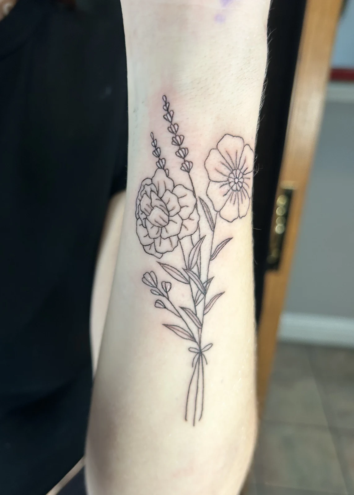 Fresh fine-line floral bouquet tattoo on a forearm