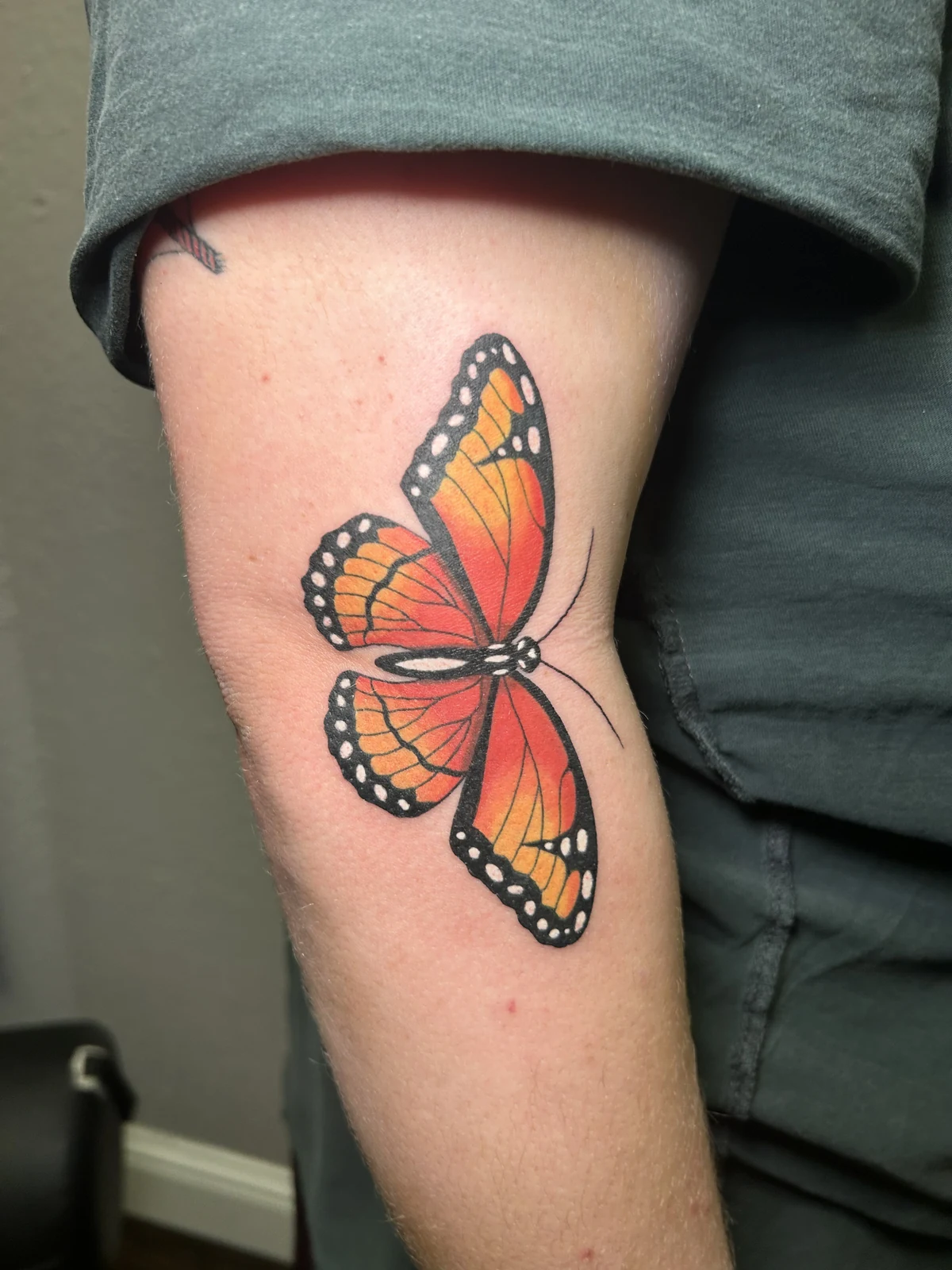 Fresh orange and black butterfly tattoo near an elbow