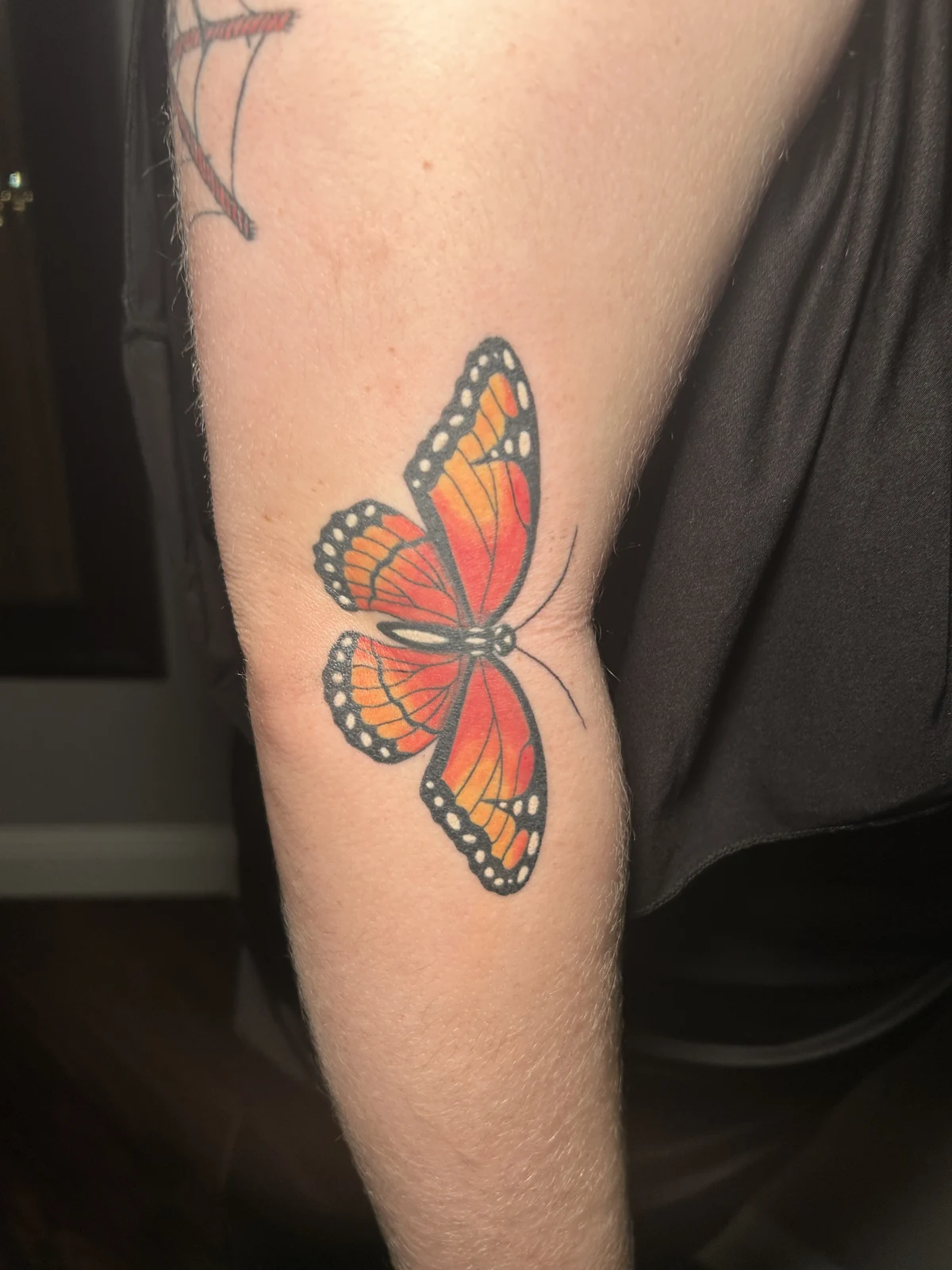 Healed orange and black butterfly tattoo near an elbow