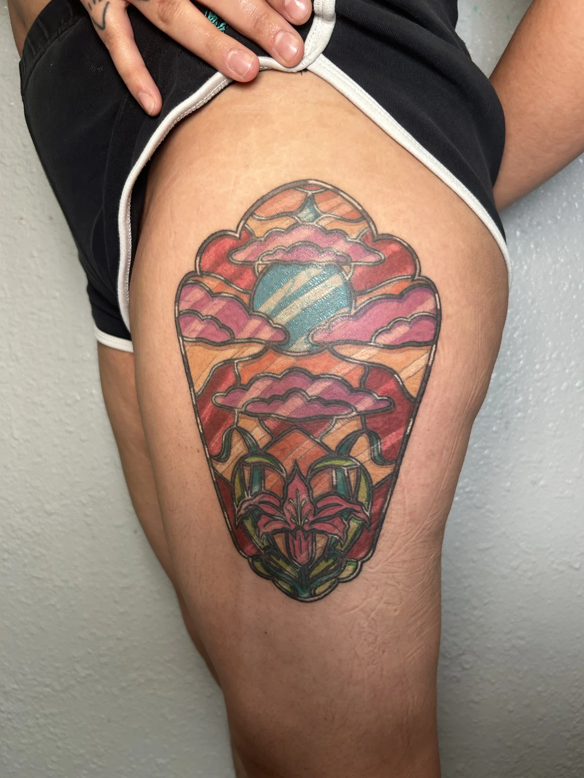 Healed stained-glass style tattoo with a planet, clouds and flowers on a thigh