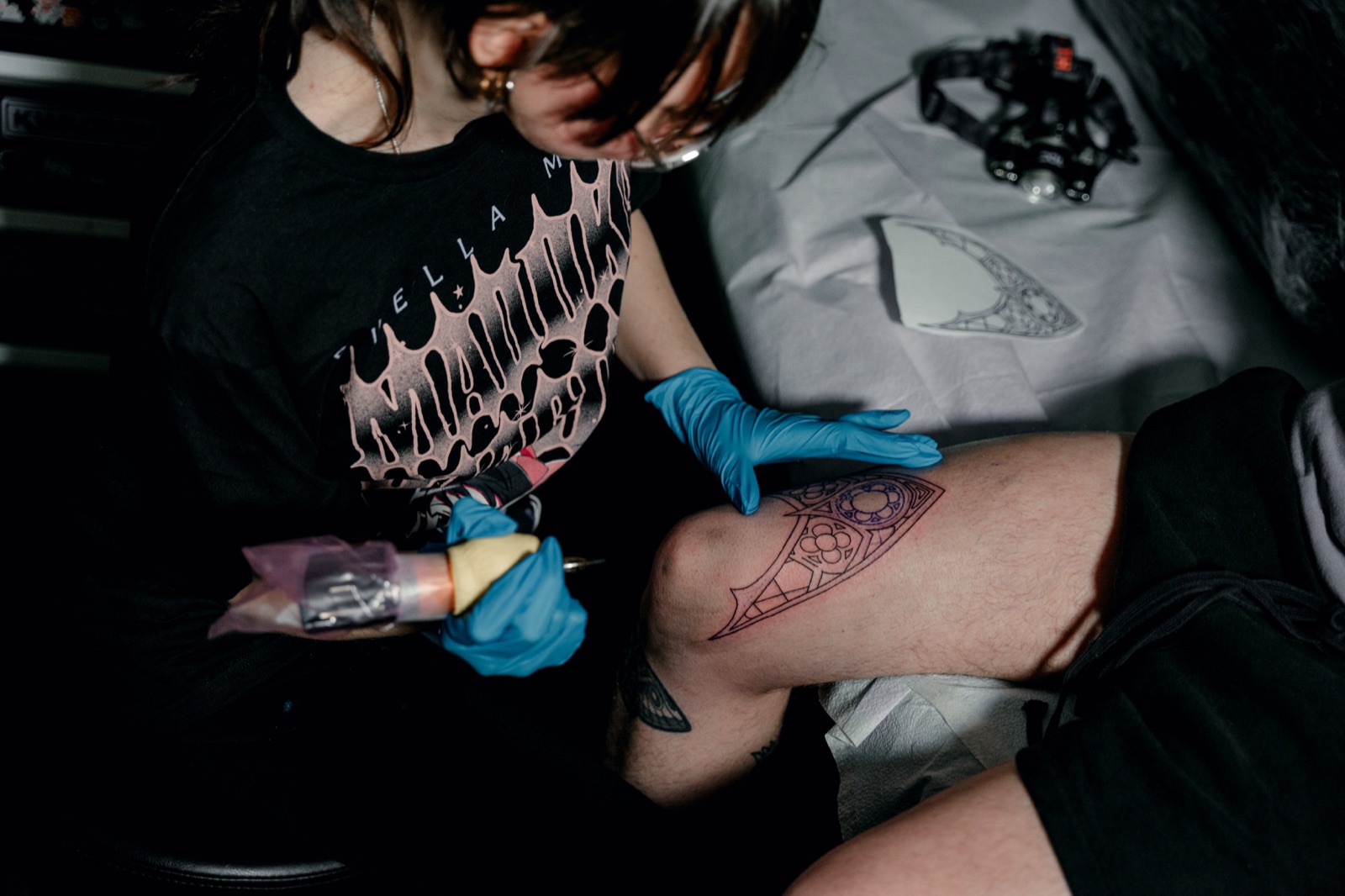 Juniper working on a tattoo in progress, with her gloved hands and the design visible